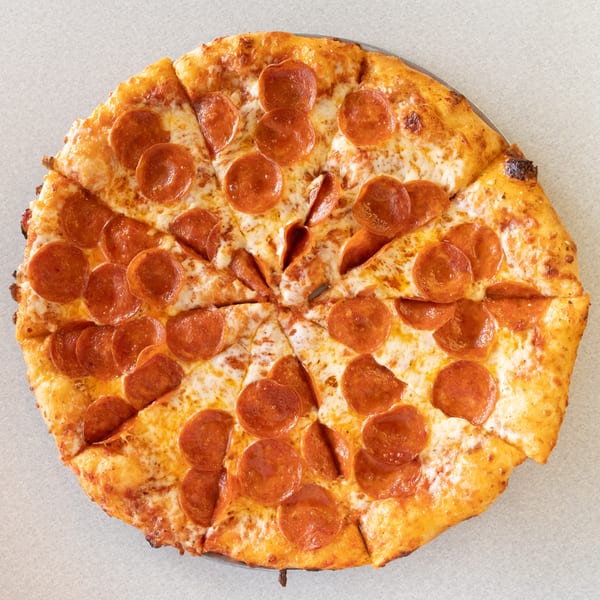 A whole pepperoni pizza, cut into slices, on a light-colored surface.