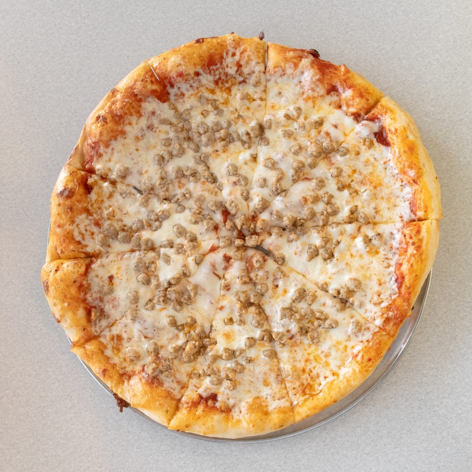 A whole sausage pizza, cut into slices, on a metal tray.