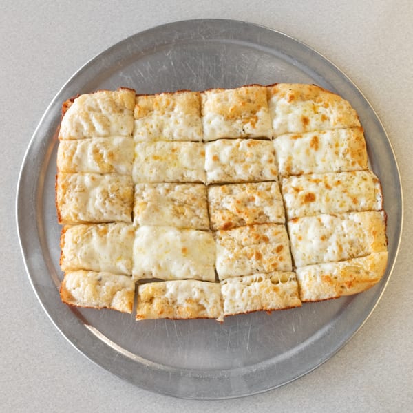 Cheesy garlic breadsticks, cut into squares, served on a round metal pizza pan.