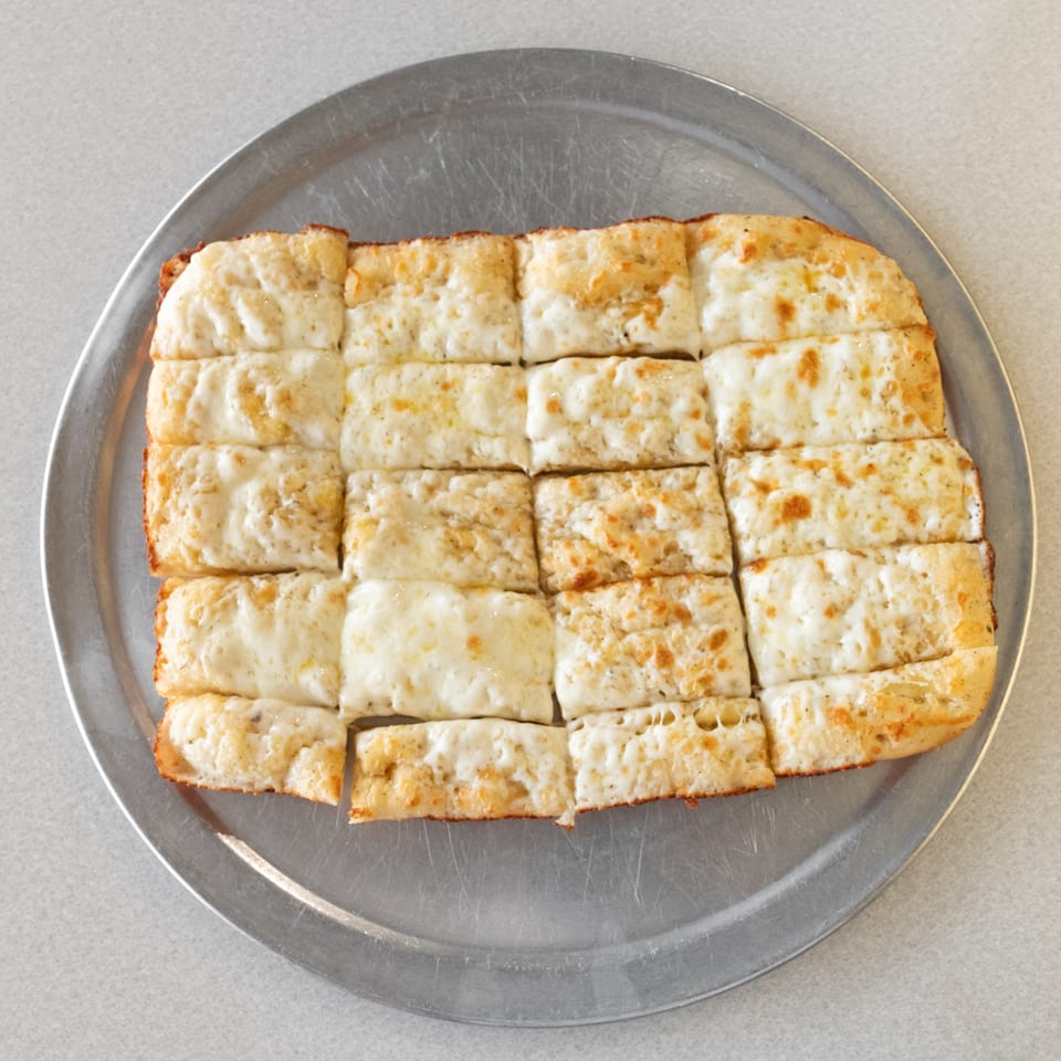 Cheesy garlic breadsticks, cut into squares, served on a round metal pizza pan.